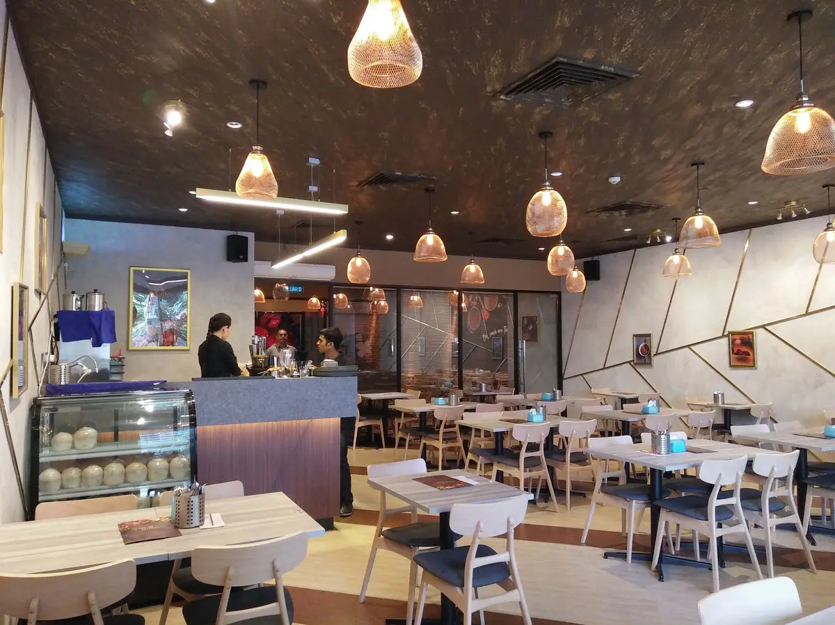 Restaurant with copper pendant lights, a service counter and pale timber tables