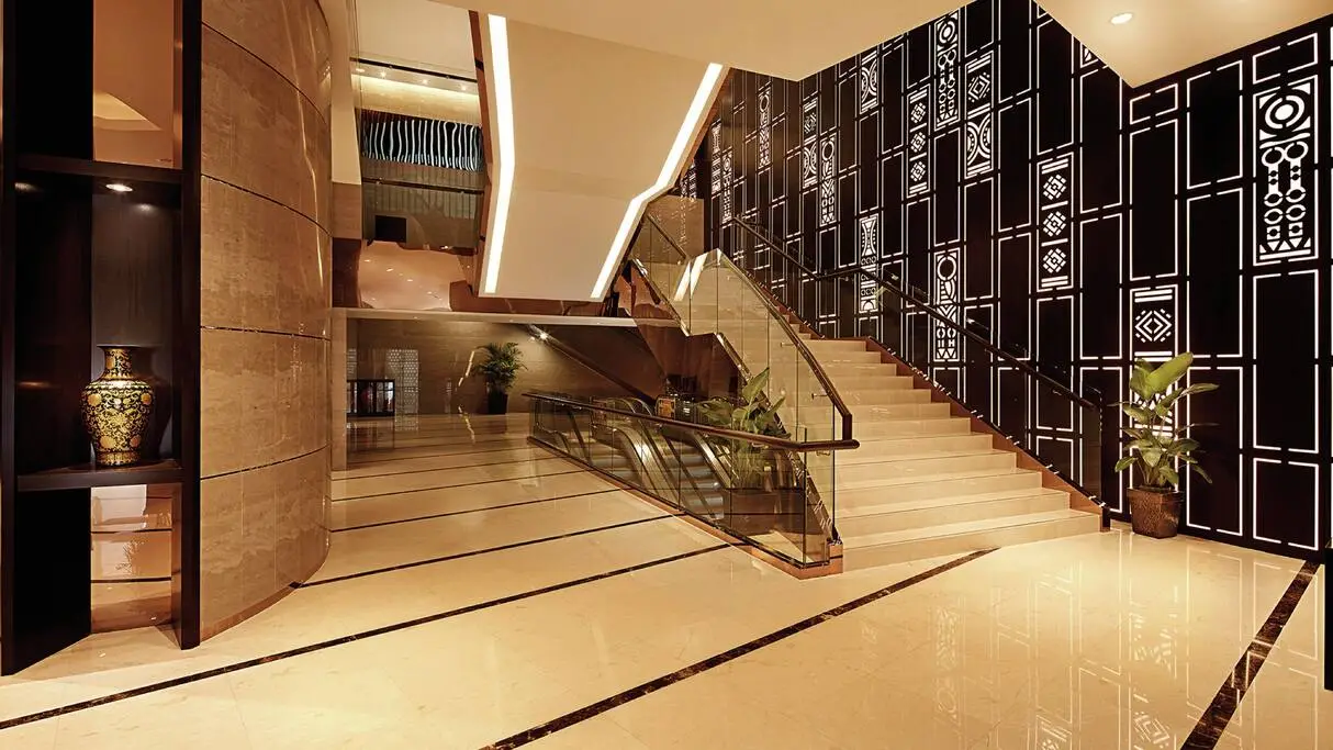 Hotel lobby stair in cream marble with glass balustrade, escalator and dark fretwork screen wall