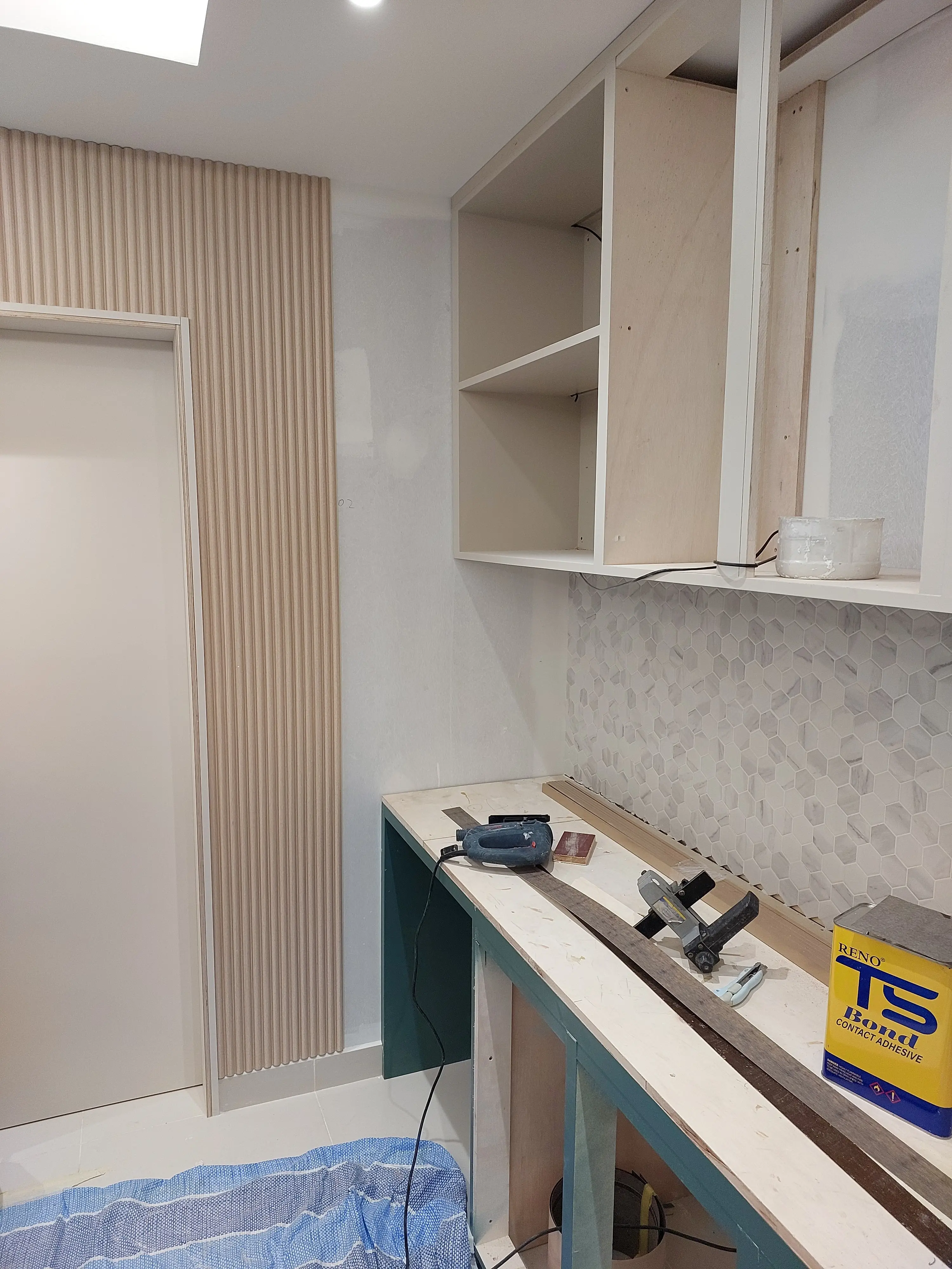 Joinery install underway: open melamine carcasses, fluted oak panel, hexagonal marble mosaic and site workbench