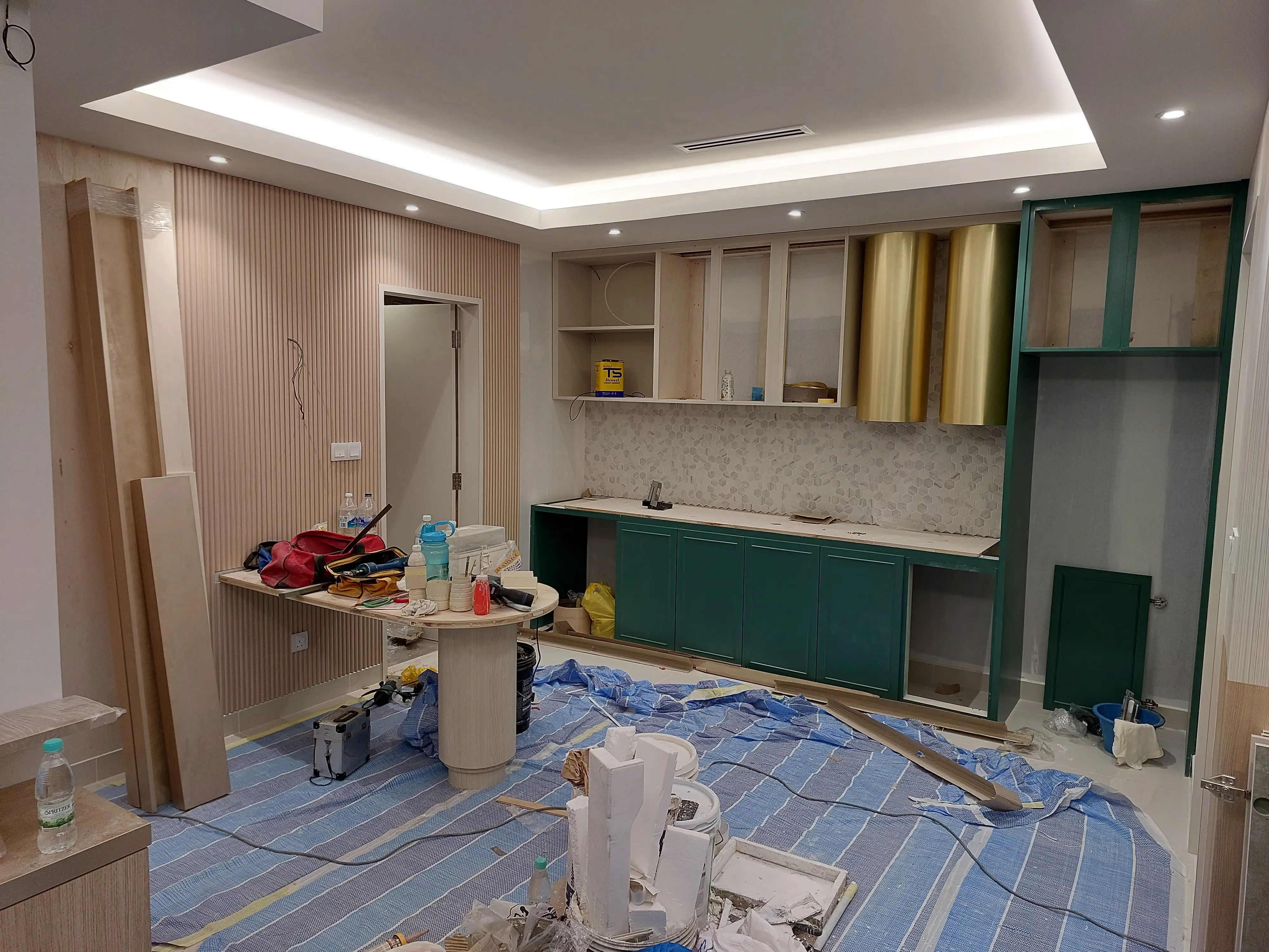 Kitchen fit-out with green shaker bases, brass cylinders, doorless upper carcasses and floor protection sheeting