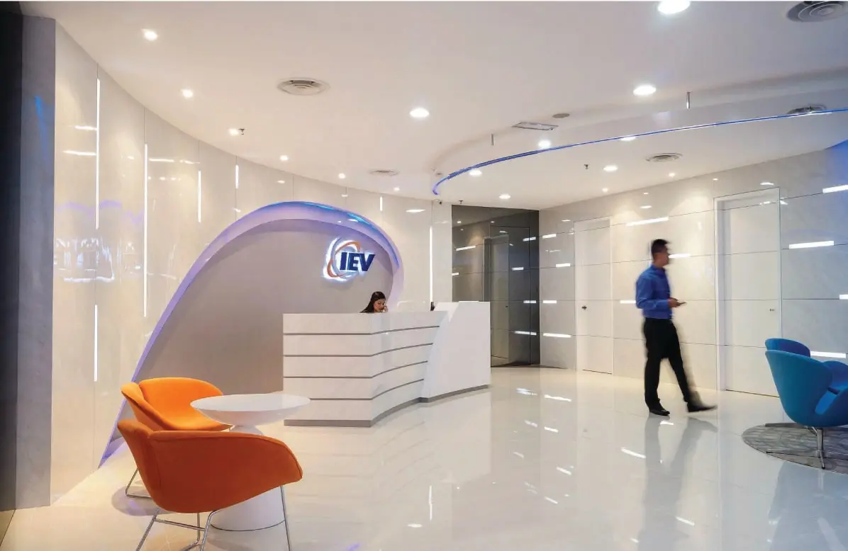 Curved reception lobby with stepped desk, illuminated IEV logo, yellow and pink tulip armchairs, polished floor