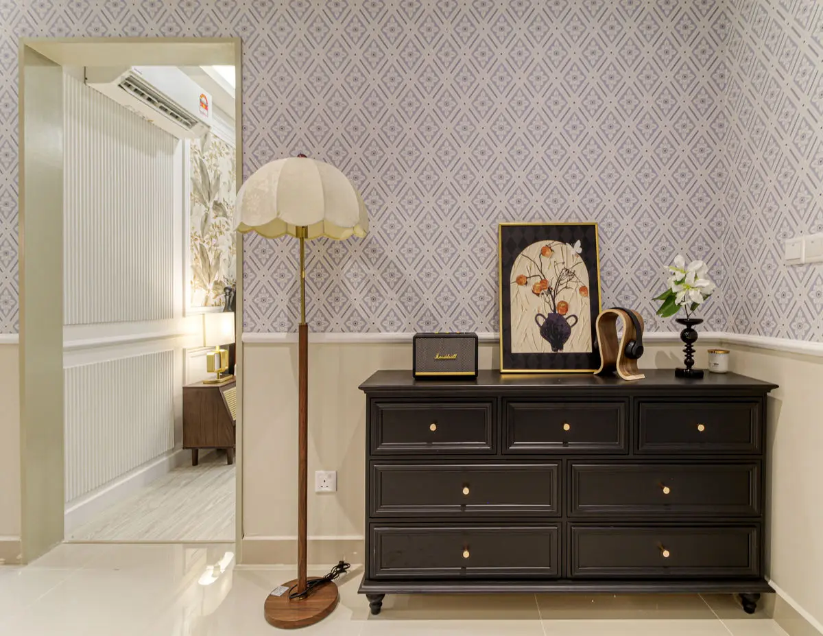 Hallway with patterned wallpaper, a dark chest of drawers and a fringed floor lamp