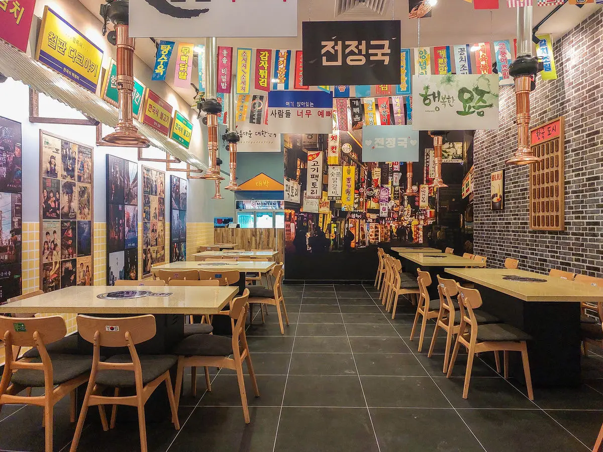 Dining room styled as a Korean street, with hanging signage and grill tables