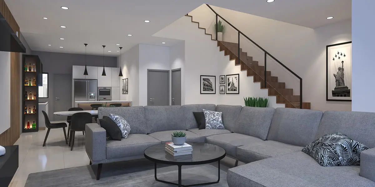 Living area with a staircase behind, grey sectional sofa and framed prints