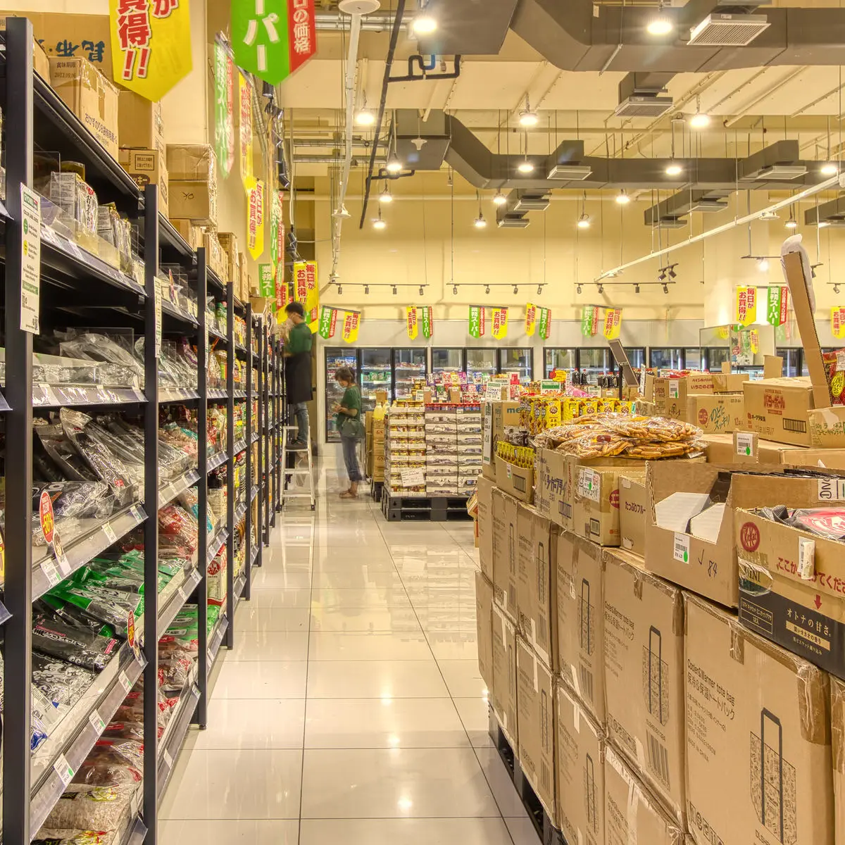Supermarket aisle with stacked cartons, shelving and hanging signage