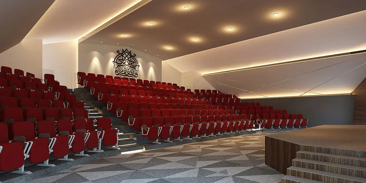 Auditorium with tiered red seating and a patterned floor