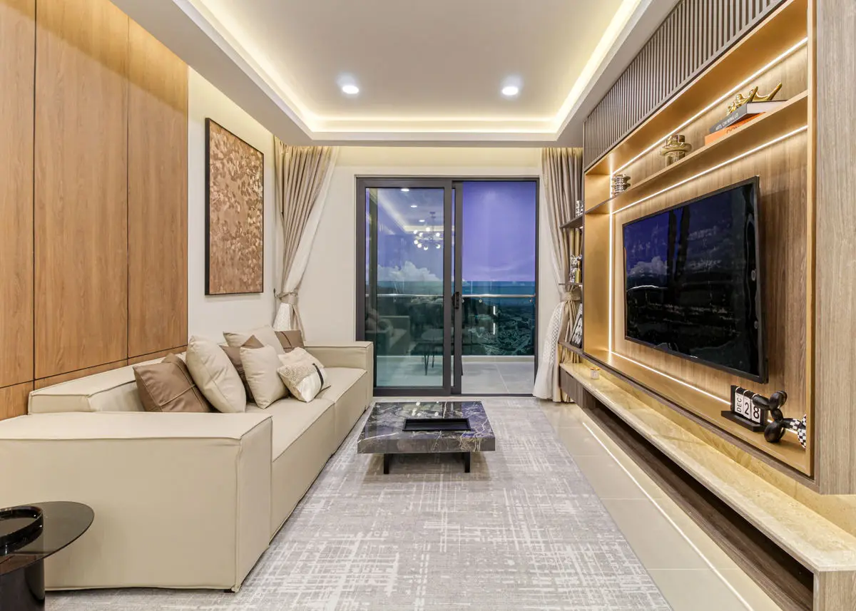 Living room with a cream sofa, backlit timber TV wall and balcony beyond