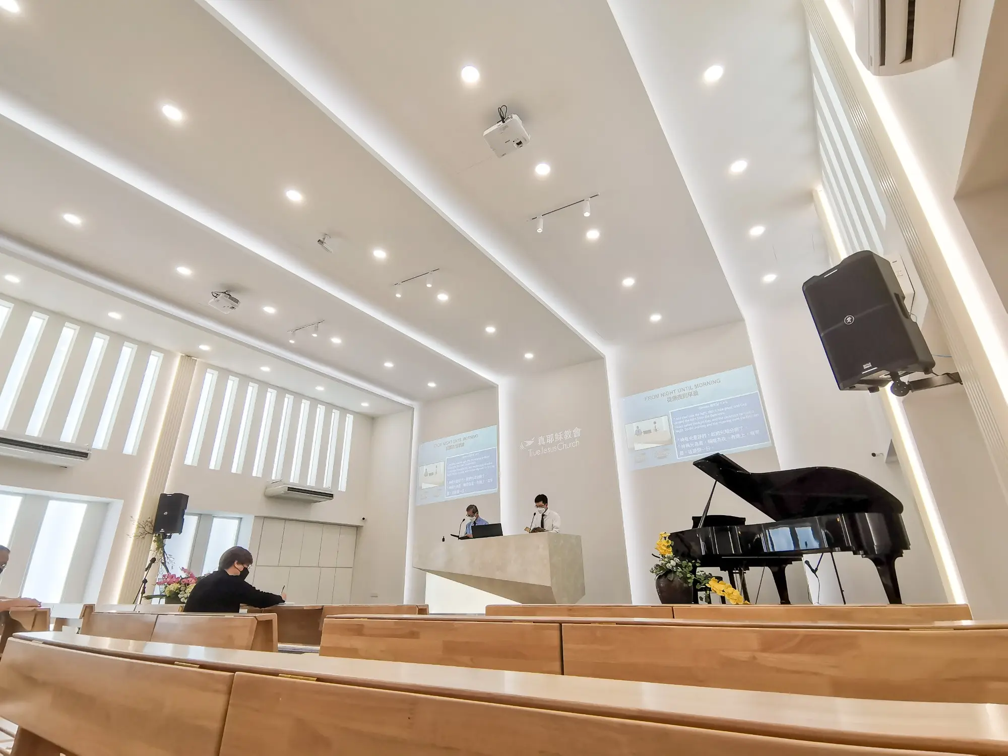 True Jesus Church hall in white plaster with cove lighting, timber pews and grand piano