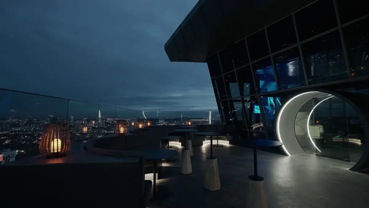 Rooftop terrace at dusk with low tables and a lit ring portal overlooking the city