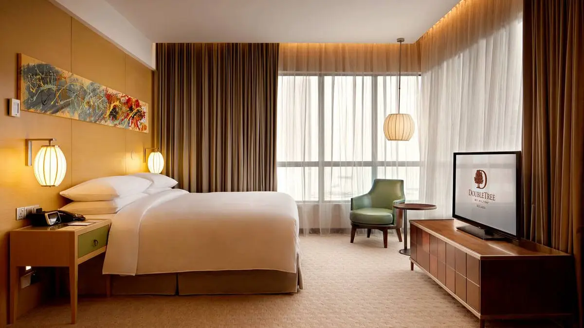Hotel guest room with a king bed, work desk and city view through sheer curtains