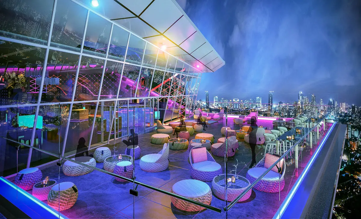 Rooftop bar at night with neon-lit seating pods and a panoramic city view