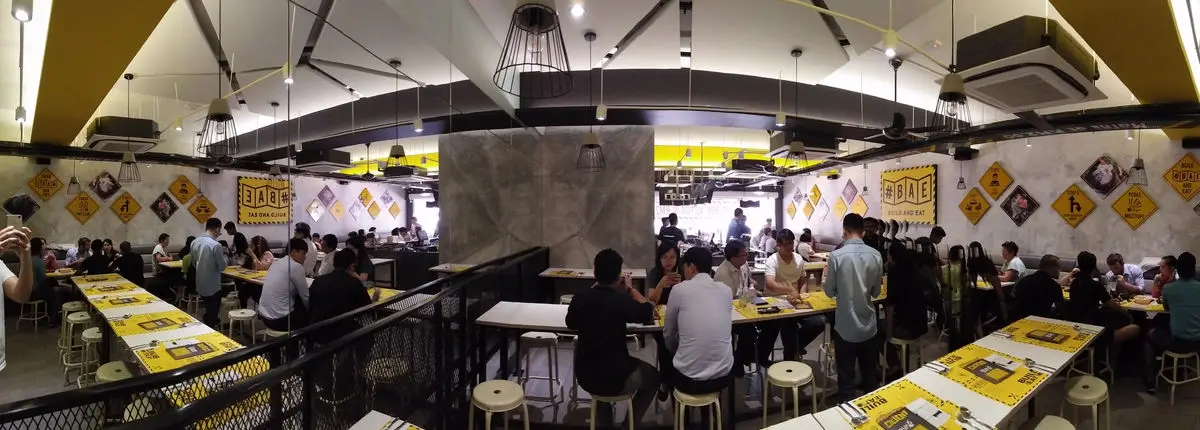 Busy dining hall with yellow-topped communal tables and an arched ceiling