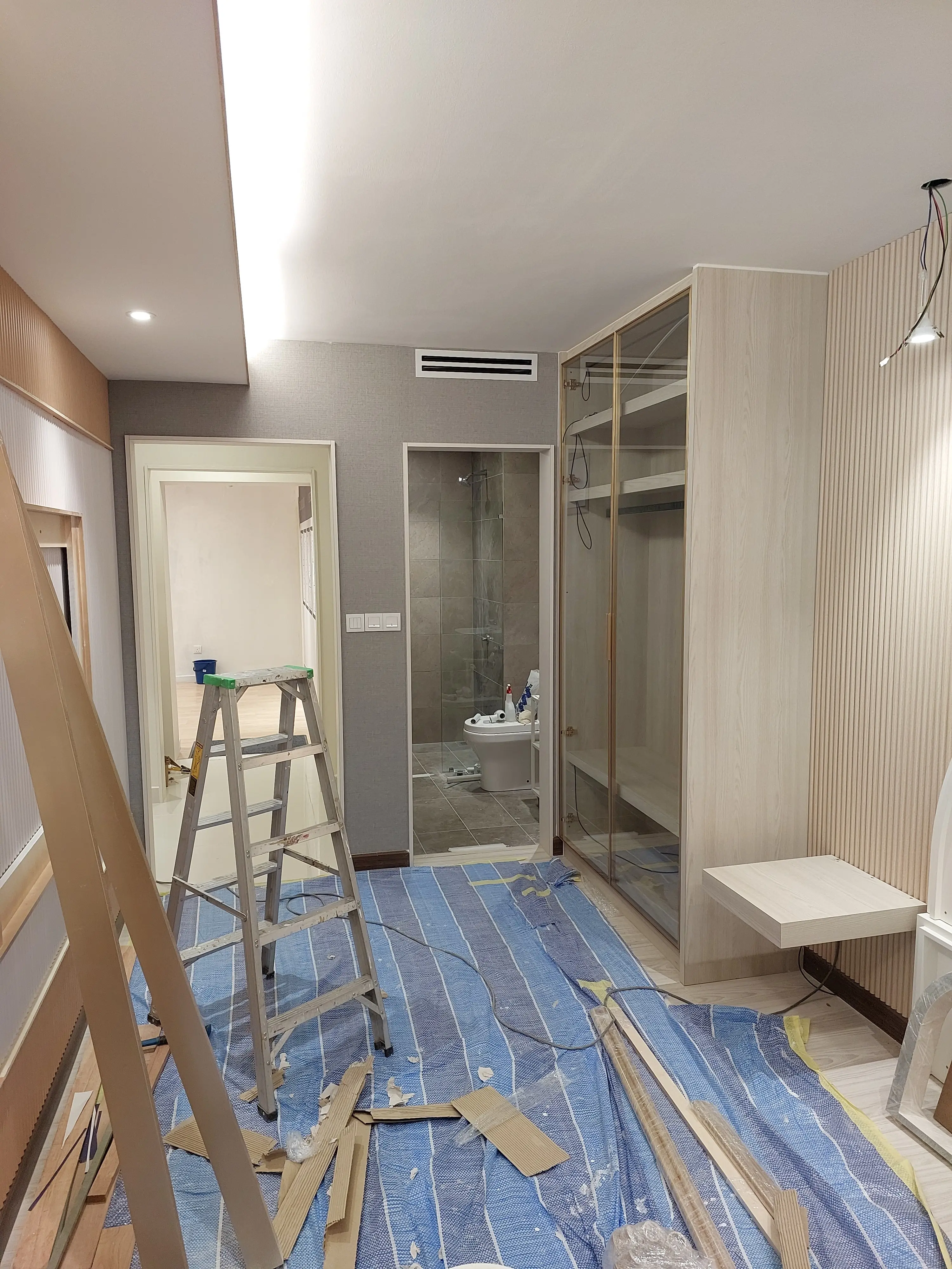 Bronze-framed glazed joinery and grey fabric panelling installed, timber offcuts and ladder on protected floor