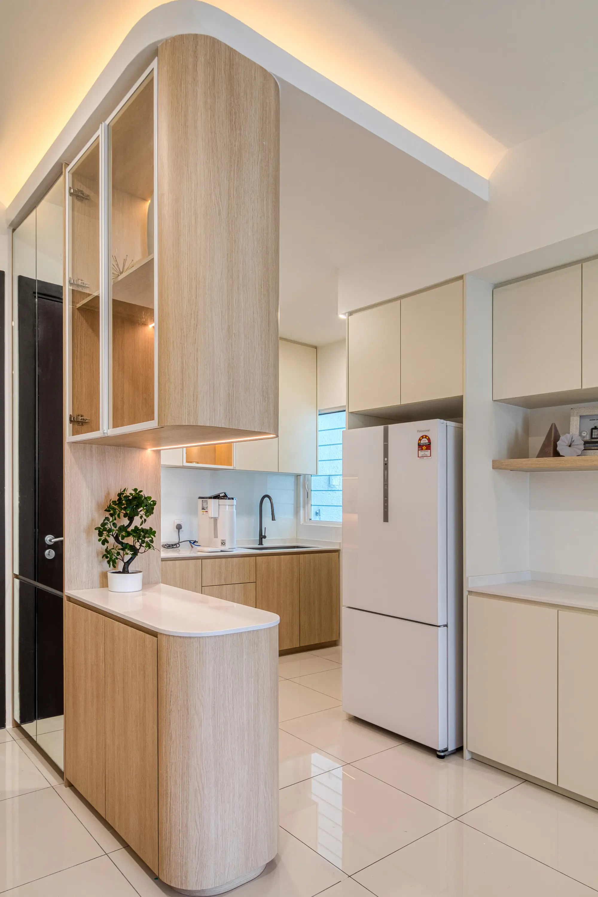 Compact white kitchen with light oak cabinetry, curved counter, glossy tiles and glass display unit
