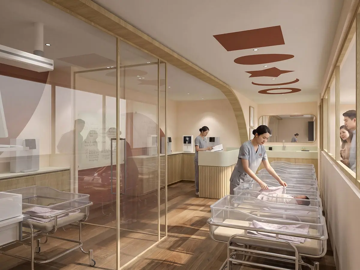 Nursery viewed through a glass partition, with a row of bassinets and staff at work