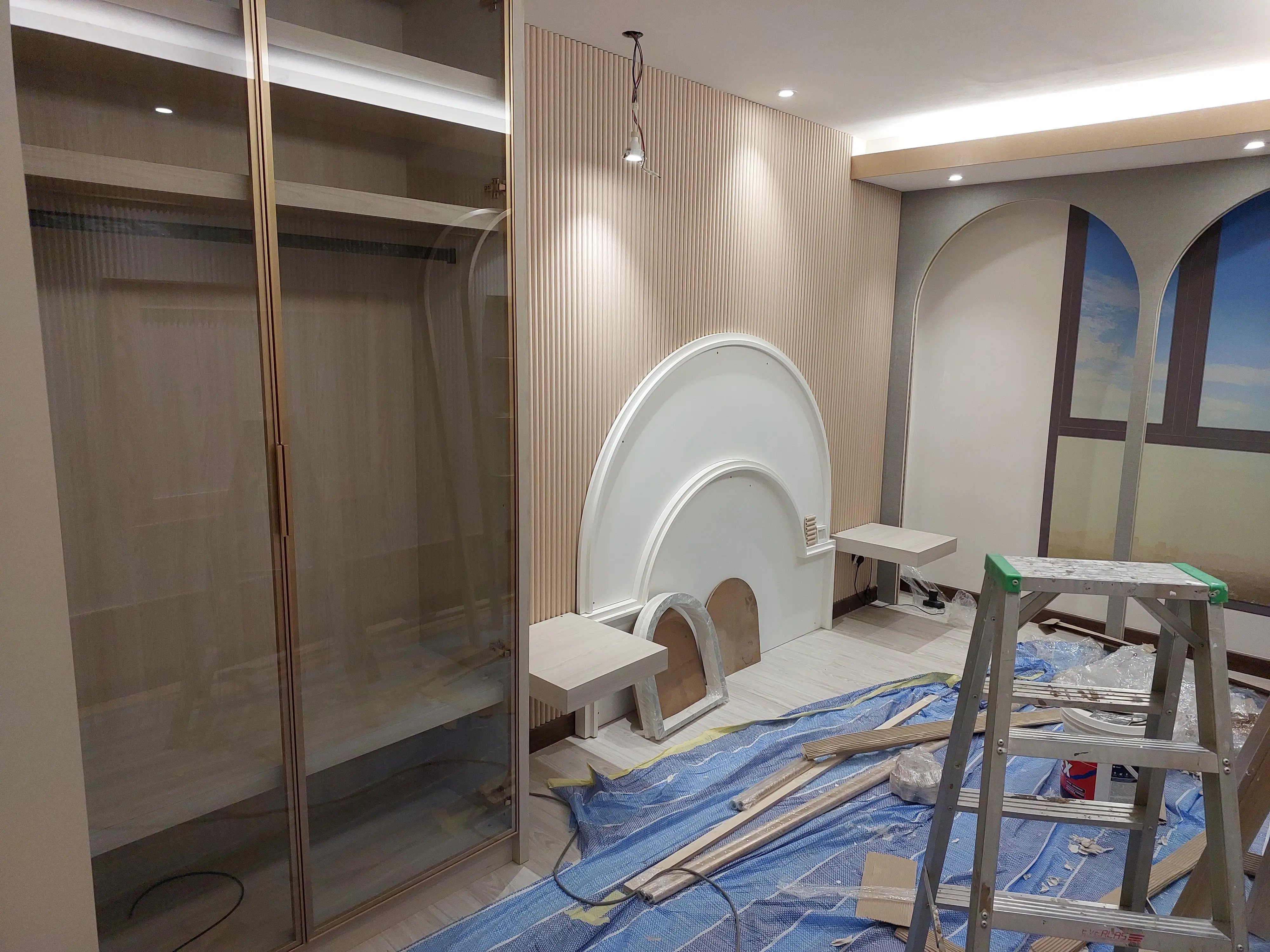 Arched white plaster niche and fluted panelling installed, reeded bronze glass doors, ladder and debris