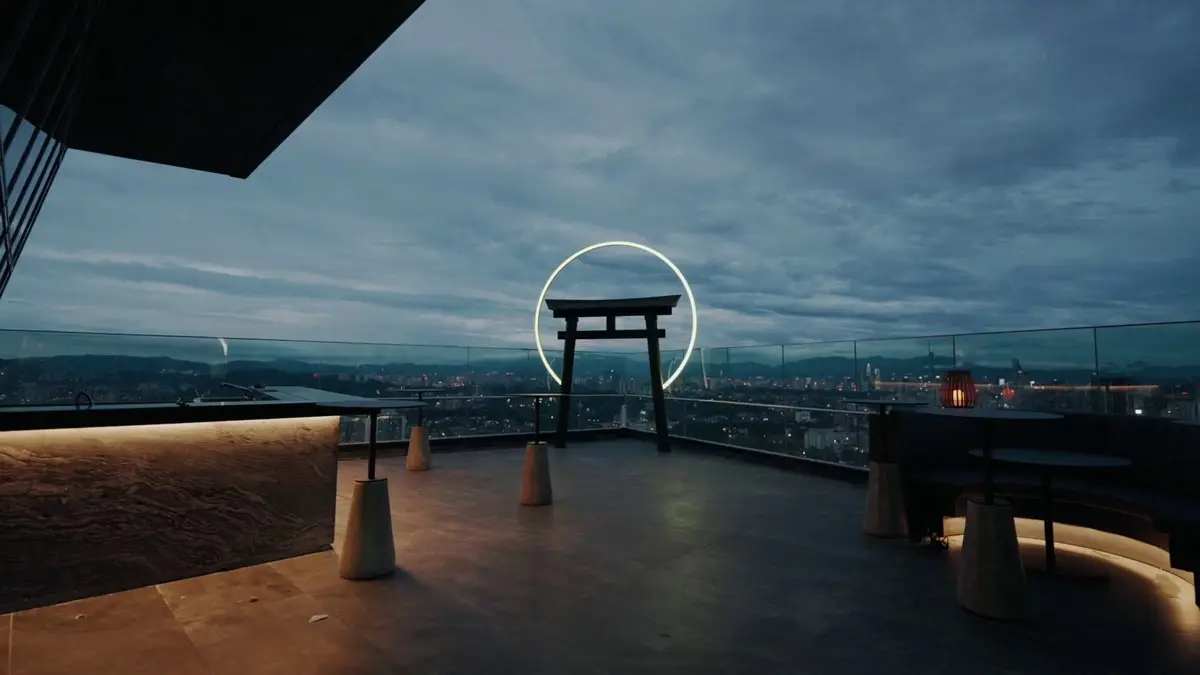 Rooftop deck with a torii gate framed by a lit ring, city lights beyond