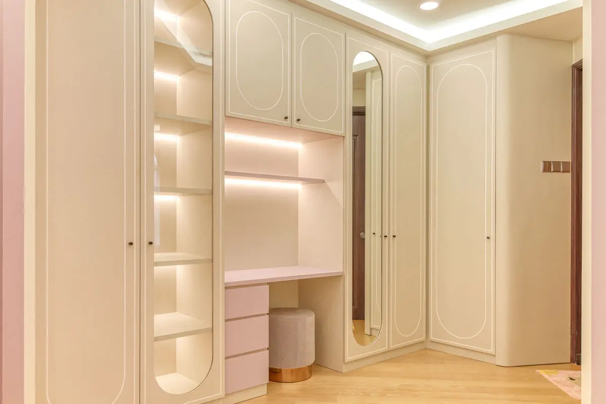 Corner dressing area with arched cabinet detailing, backlit shelving and a stool