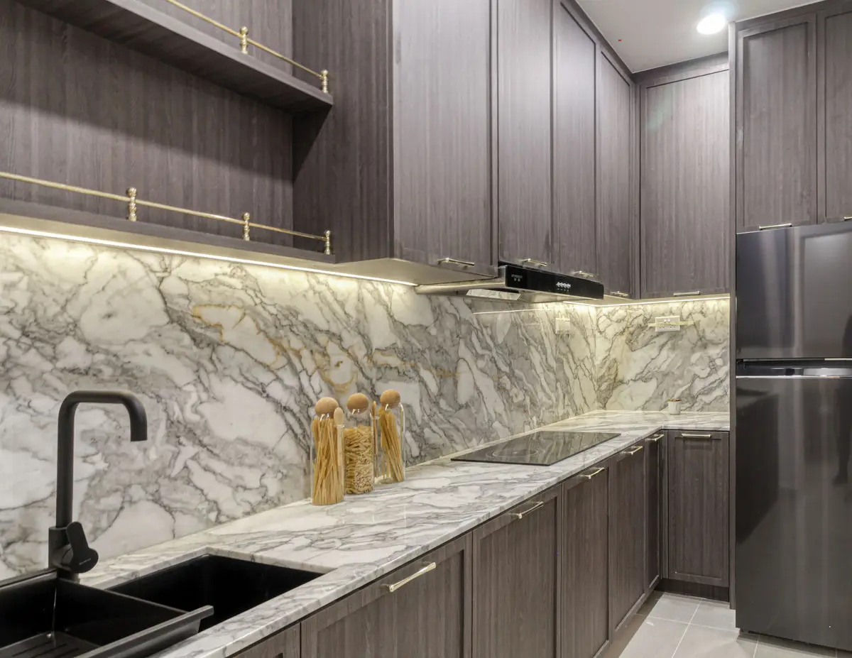 Kitchen counter detail with a marble backsplash, black sink and dark timber cabinetry