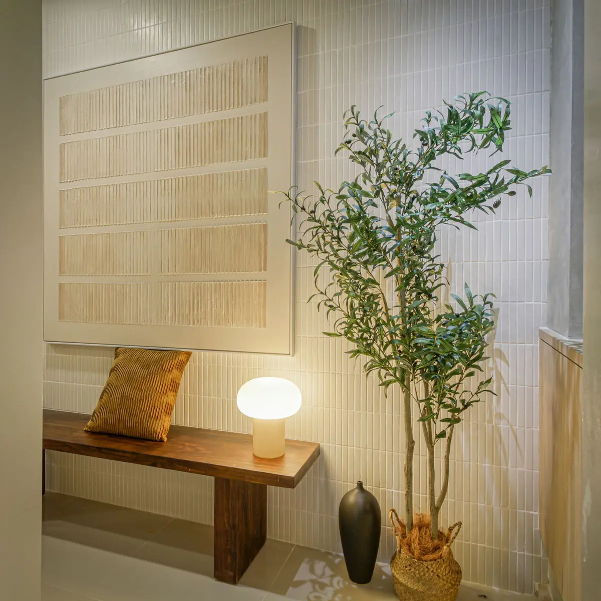 Entrance detail with a timber bench, tiled wall, table lamp and a potted olive tree
