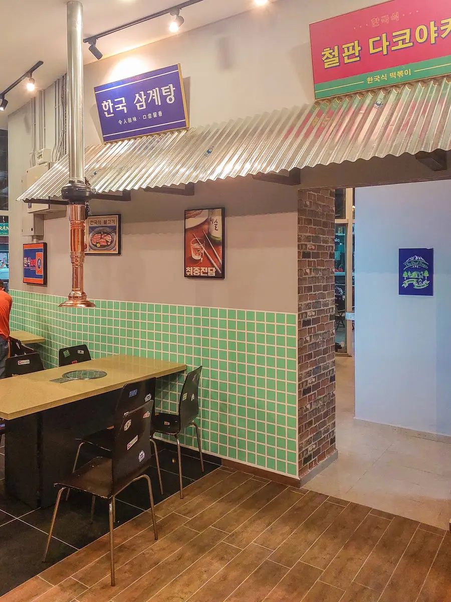 Corner booth with a grill table beneath a corrugated metal canopy