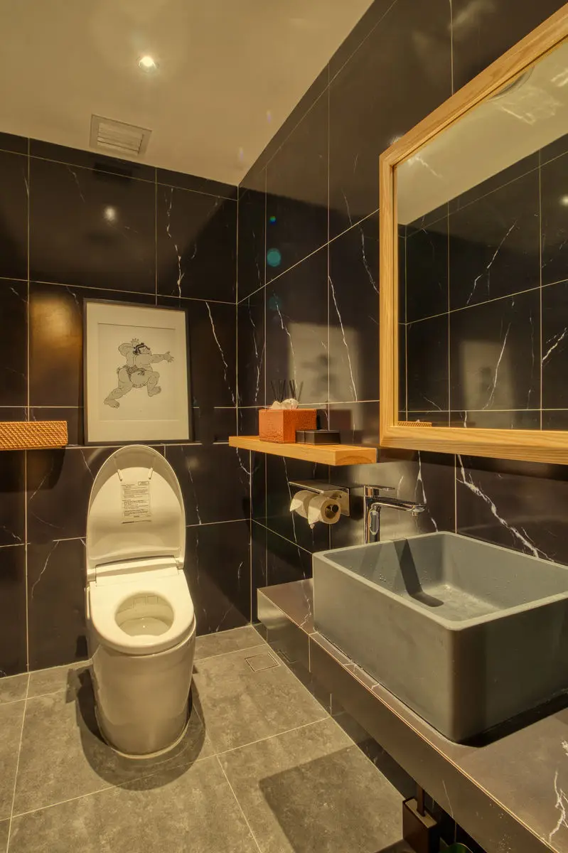 Washroom with dark marble tiling, a vessel basin and framed artwork