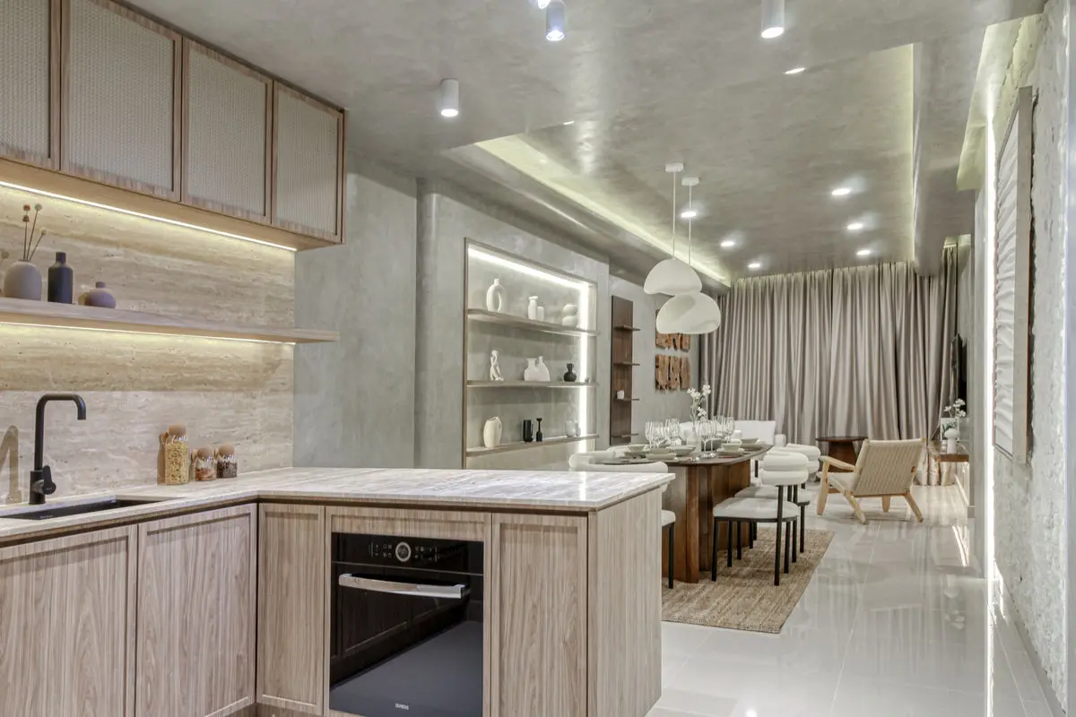 Kitchen with pale timber cabinetry, stone worktop and open shelving, dining area beyond