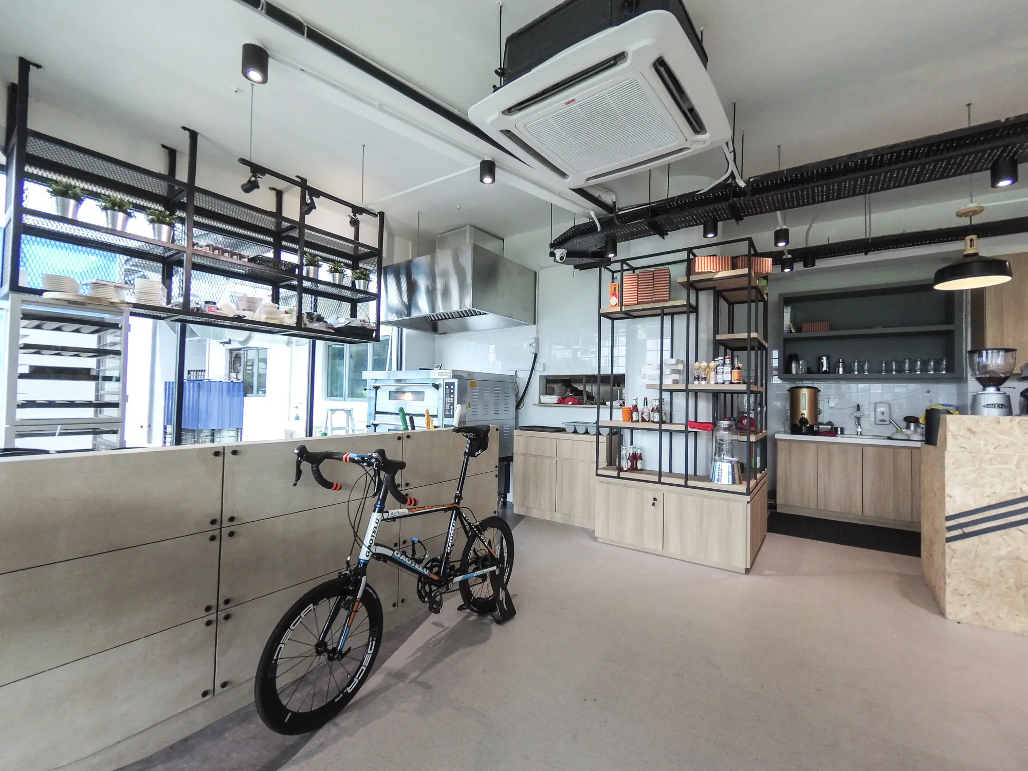 Industrial cafe kitchen with black mesh shelving, plywood counters, deck oven and stainless hood