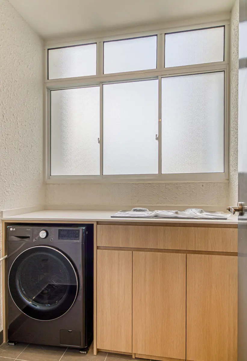 Utility area with a front-load washing machine under a timber counter, frosted windows above
