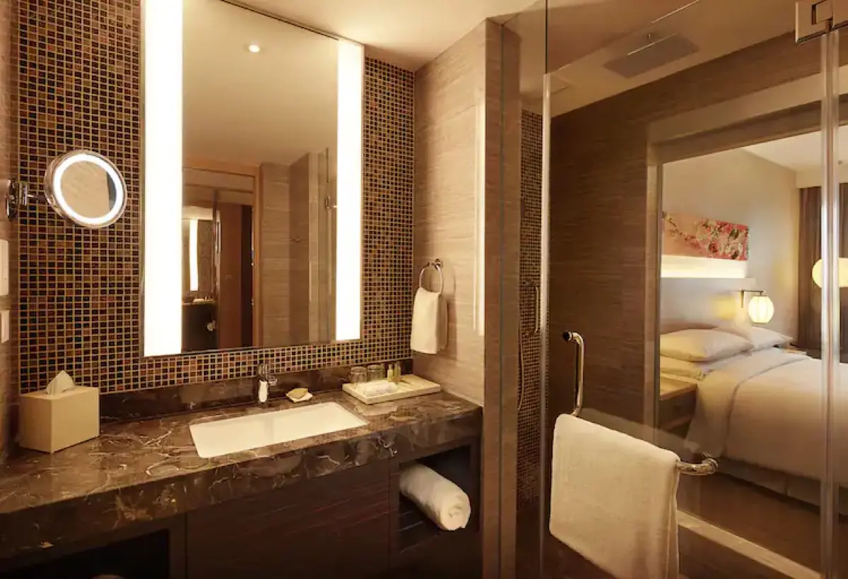 Bathroom vanity with a backlit mirror, mosaic tiling and a view through to the bedroom
