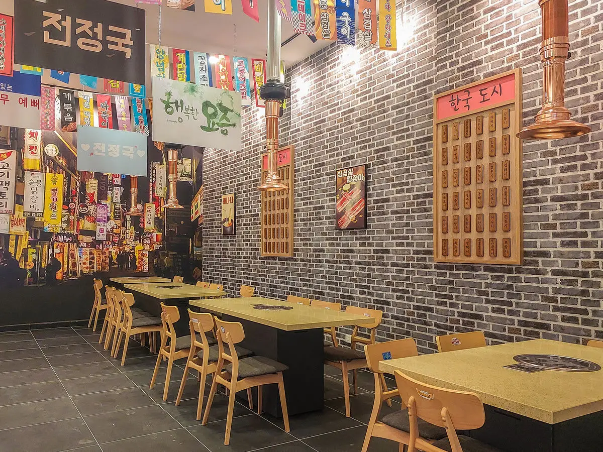 Grill tables beneath hanging signboards and copper extraction ducts