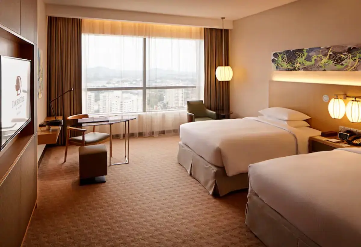 Twin-bed guest room with a work desk, armchair and window overlooking the city