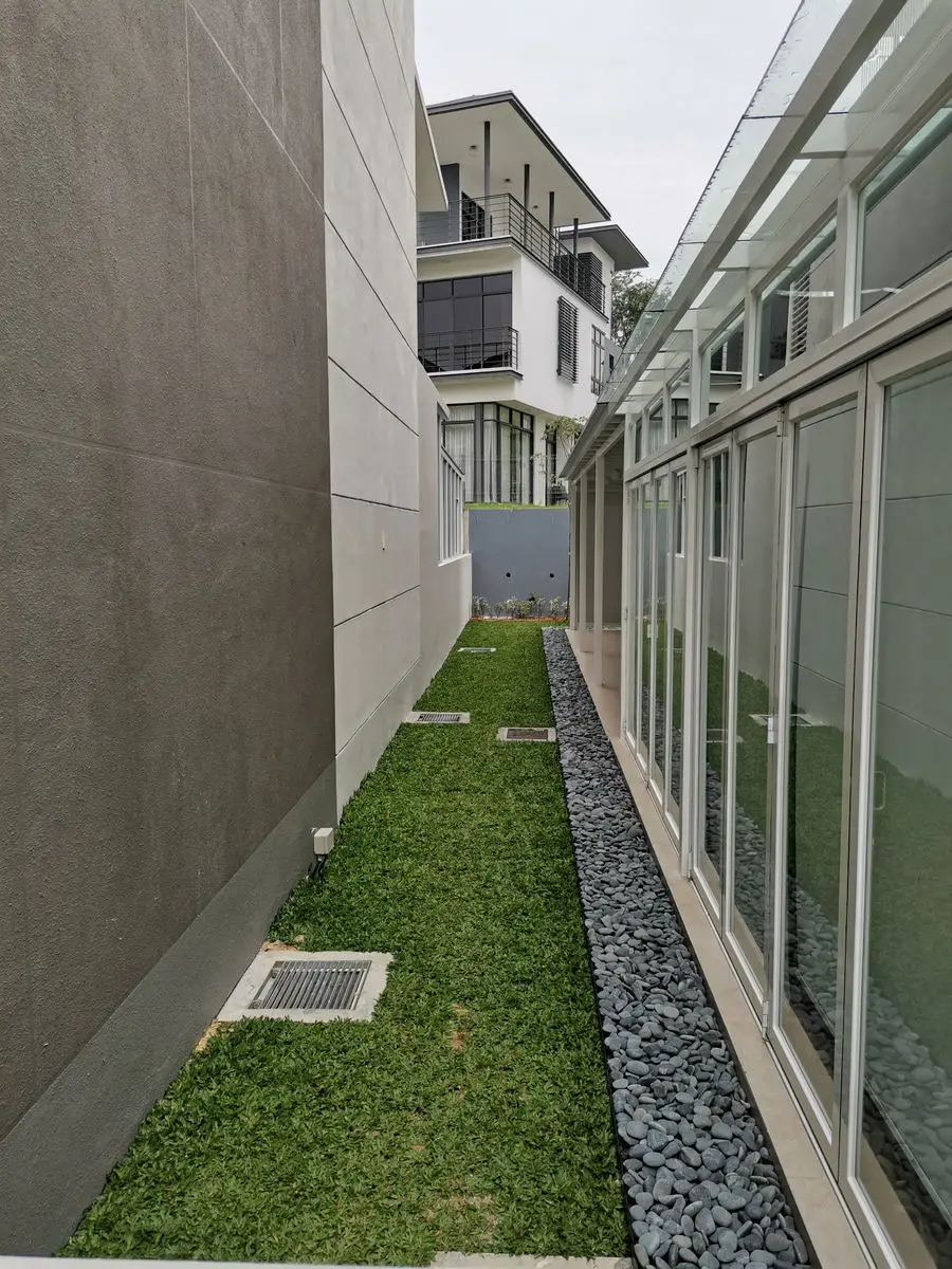 Narrow side yard with a strip of turf and pebble drainage border between two houses