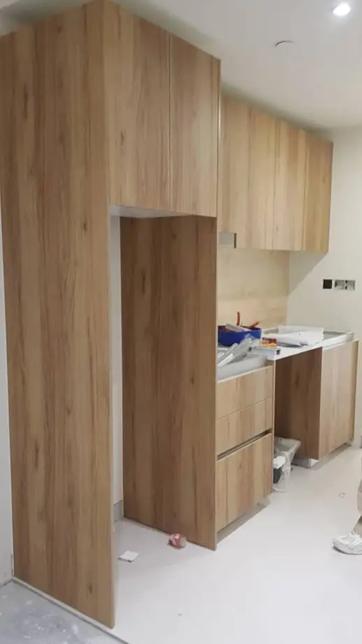 Oak-effect laminate kitchen carcasses newly fitted against stone backsplash, unfinished worktop and protected floor