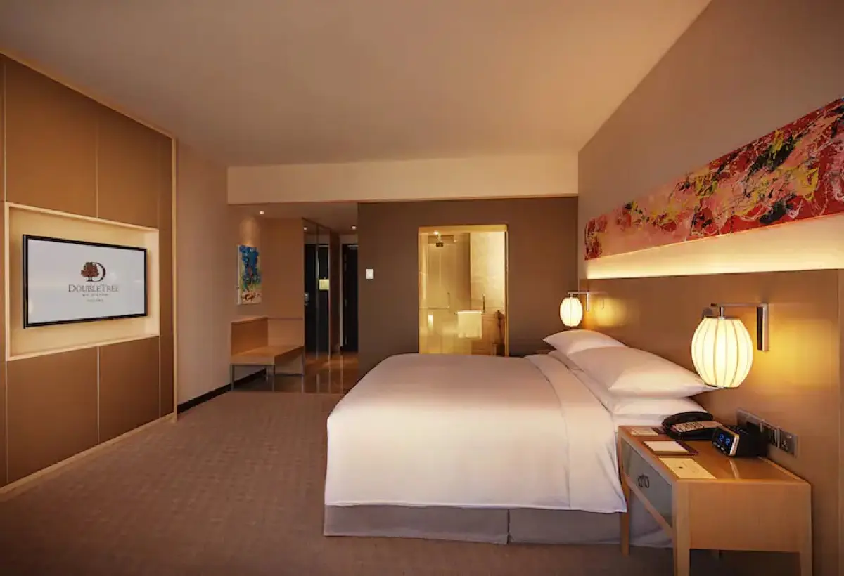 Guest room with a king bed, backlit artwork panel and a bedside reading lamp