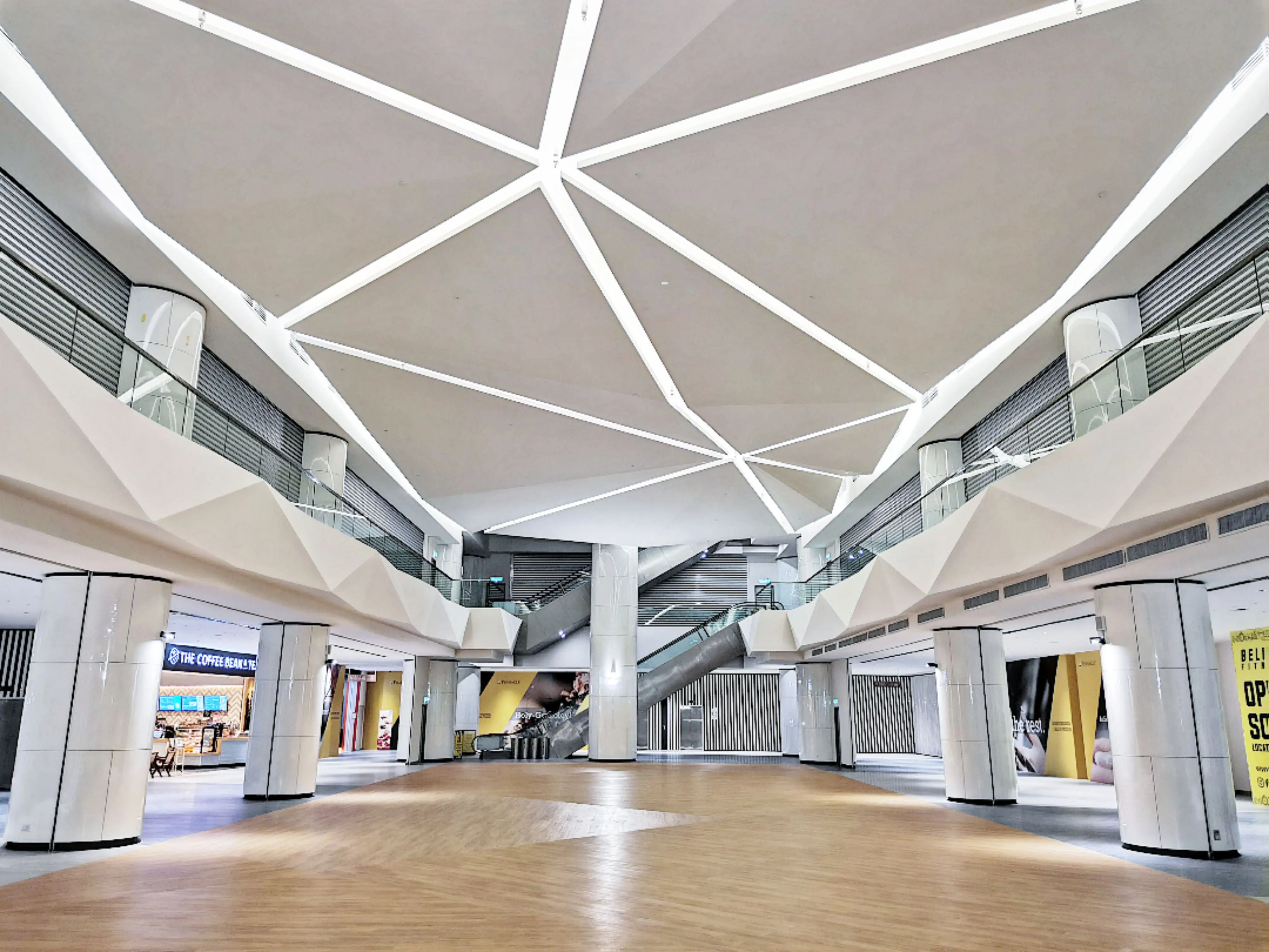 Mall concourse with faceted white ceiling, linear light strips, curved columns and timber floor