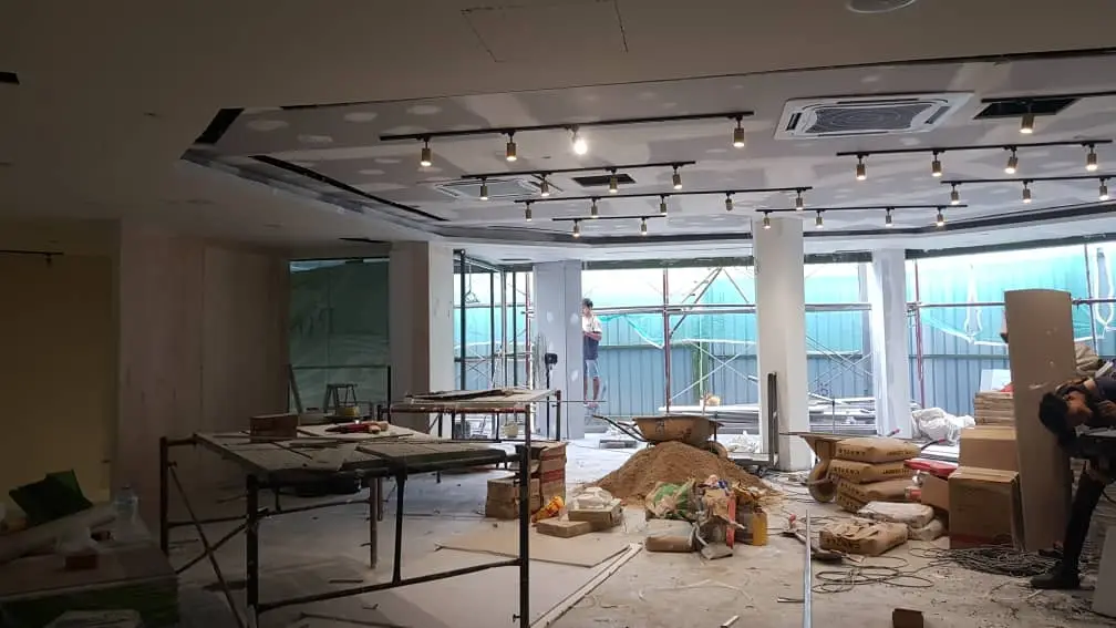 Commercial shell fit-out: track-lit plasterboard bulkhead, trestles, sand heap, cement bags and scaffolded glazing