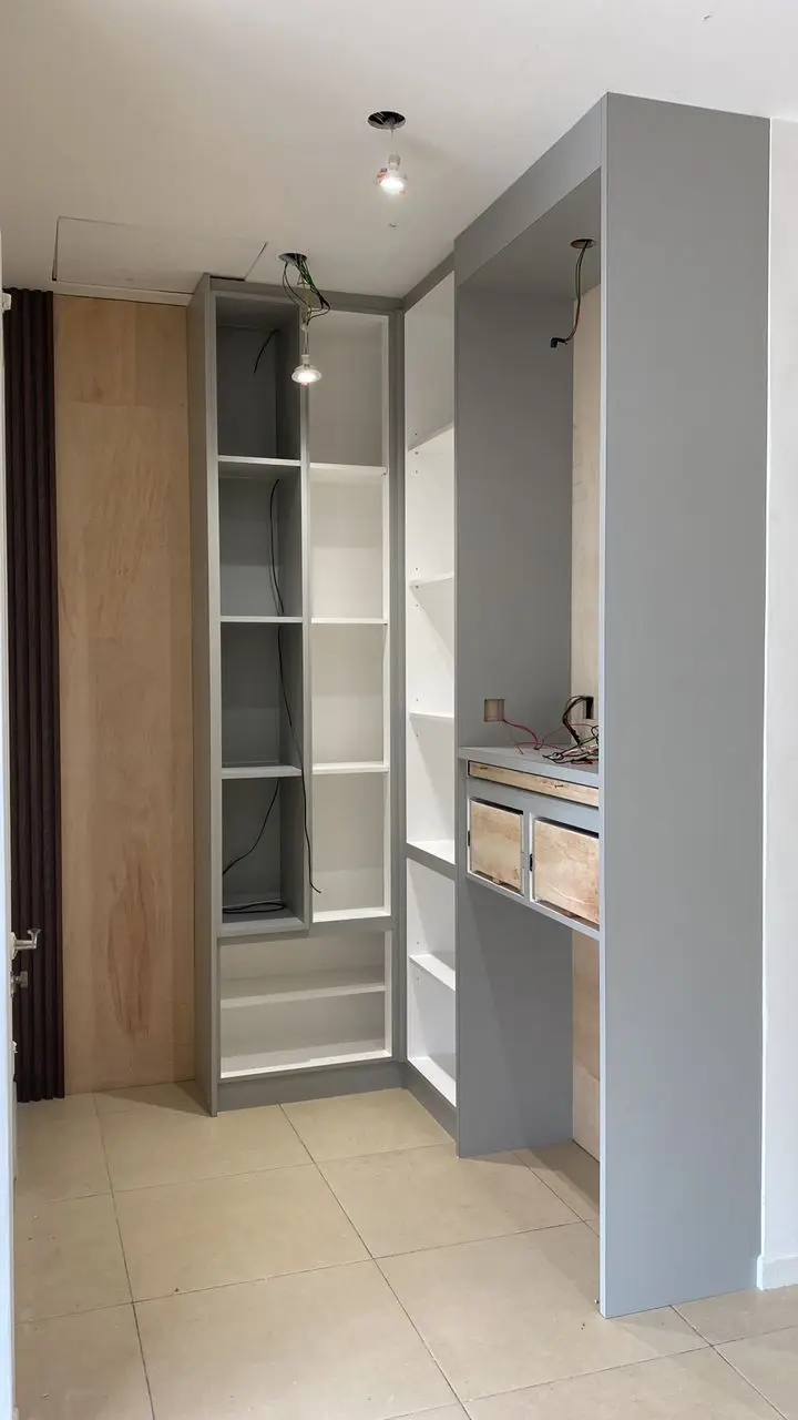 Grey painted shelving carcass under construction with plywood back, bare pendant lamp and loose wiring