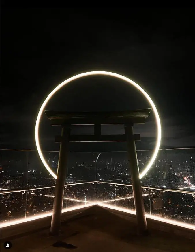 Torii gate and illuminated ring on the rooftop, overlooking the city at night